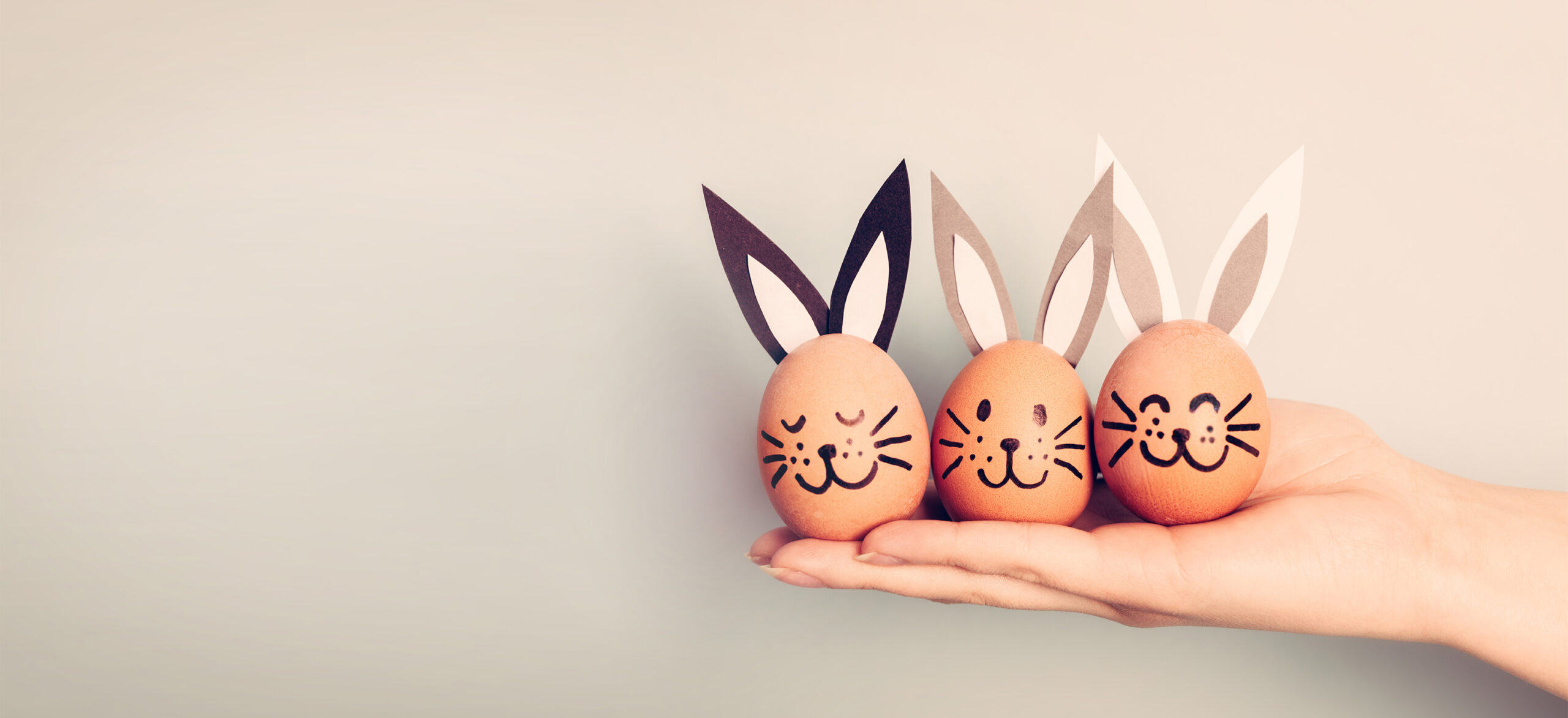 Drei bemalte Eier mit Hasengesichtern und Papierohren liegen auf einer ausgestreckten Hand.
